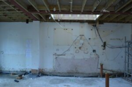 The image shows a construction site with exposed wooden beams, exposed plaster walls, and various tools and equipment scattered around.
AI-generated content may be incorrect.